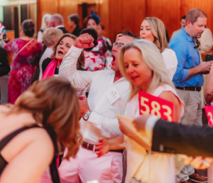 A festive crowd playing spin to win with people cheering and mingling.
